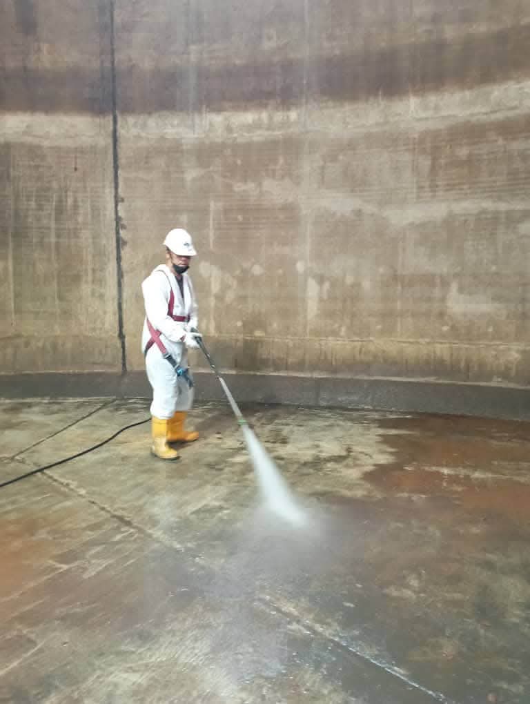 Crew member pressure washing inside a tank